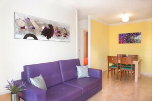 Un sofà morat, una taula de dinar amb cadires i un quadre a la paret.