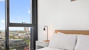 Une chambre d’hôtel dotée d’une grande fenêtre, d’un lit avec une literie blanche, d’une table de chevet avec une lampe et offrant une vue sur le paysage urbain.