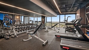 Une salle de sport équipée de tapis de course, d’haltères et d’appareils de musculation, avec de grandes fenêtres et une vue sur la ville.