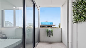 Una habitación de hotel moderna con una cama, una puerta de vidrio, vista a un edificio con un cartel y una planta en maceta.