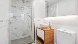 Un baño moderno con ducha envuelta en vidrio, tocador de madera y inodoro blanco.