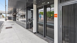 Fachada moderna de un edificio con puertas de vidrio, una cámara de seguridad y un detector de incendios visible.