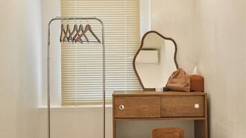 Une chambre à coucher avec une commode en bois, un miroir, une table de chevet, une chaise et une lampe sur pied.