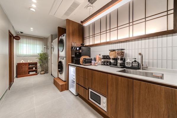 A modern kitchen with built-in appliances, a sink, and a window with blinds. - Hongdae Ongi Hotel (Seoul)