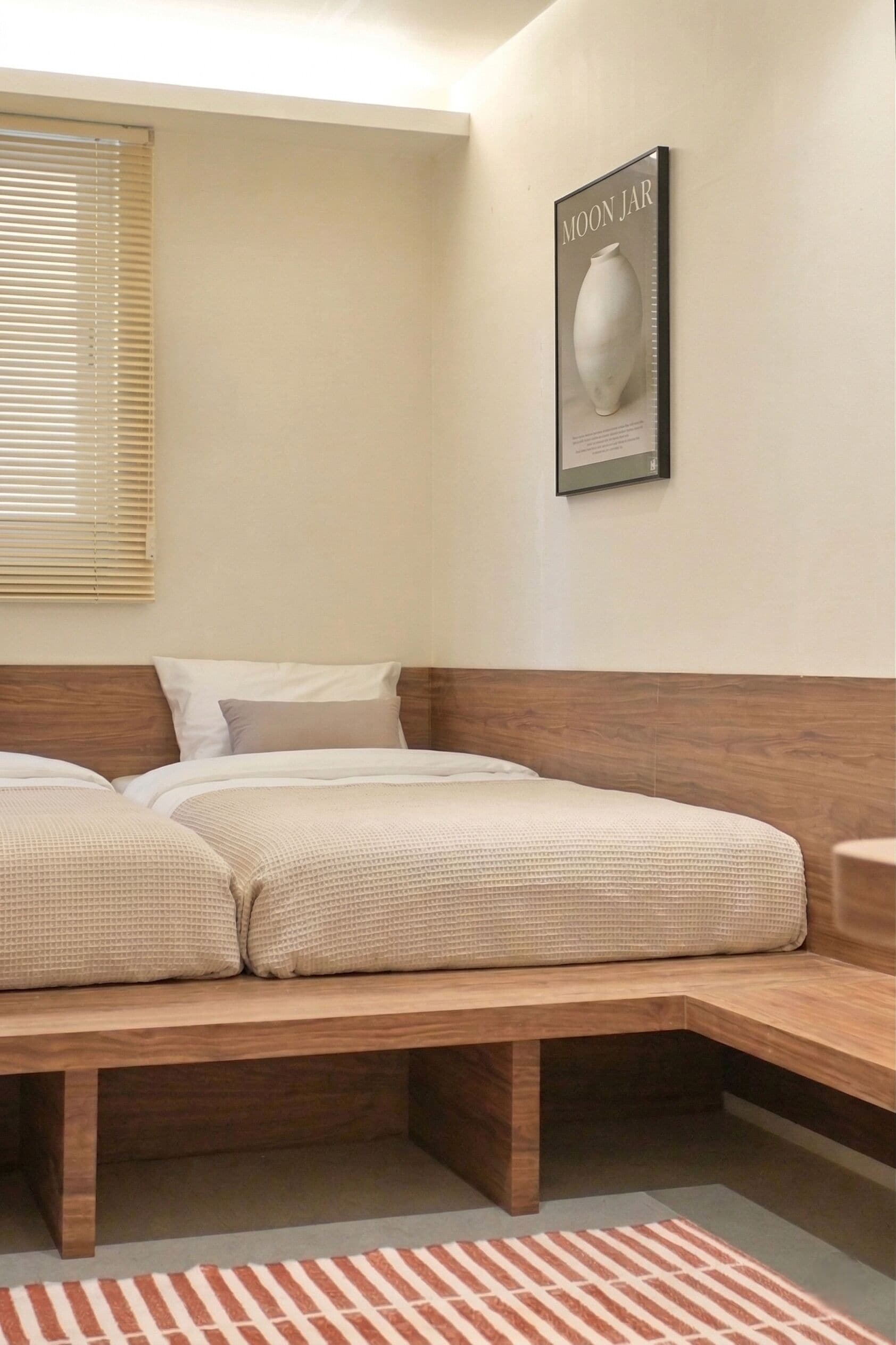 A bedroom with a wooden bed, a headboard, a window with blinds, and a framed picture on the wall.