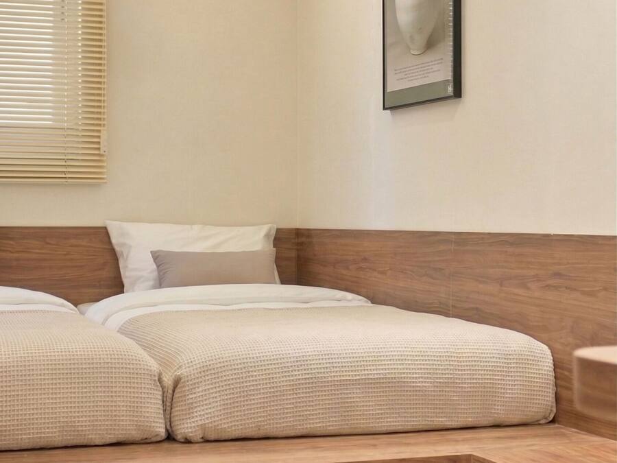 A bedroom with a wooden bed, a headboard, a window with blinds, and a framed picture on the wall.