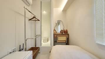 Une petite chambre à coucher comprenant un lit, une commode en bois, un miroir et un espace douche.