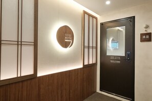 A hotel reception area with a wooden panel wall, a circular sign with 'ONGI HOTEL' text, a welcome sign on the door, and a digital display. - Hongdae Ongi Hotel (Seoul)