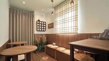 A restaurant interior with wooden tables and chairs, a window with a grid pattern, and a wall-mounted shelf with round objects.