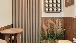 A modern interior with wooden flooring, a round table with chairs, a small round table, a wall-mounted shelf with decorative items, and a curtain. - Hongdae Ongi Hotel (Seoul)