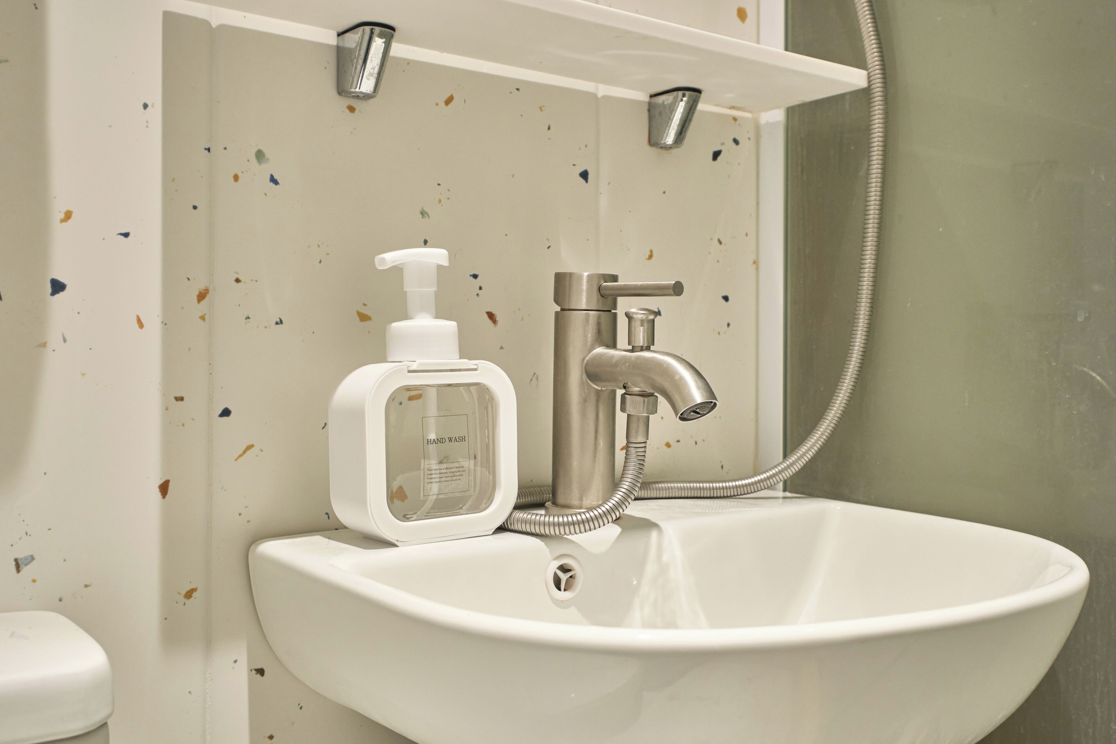 A bathroom with a white sink, a hand soap dispenser, a faucet, and a shower head.