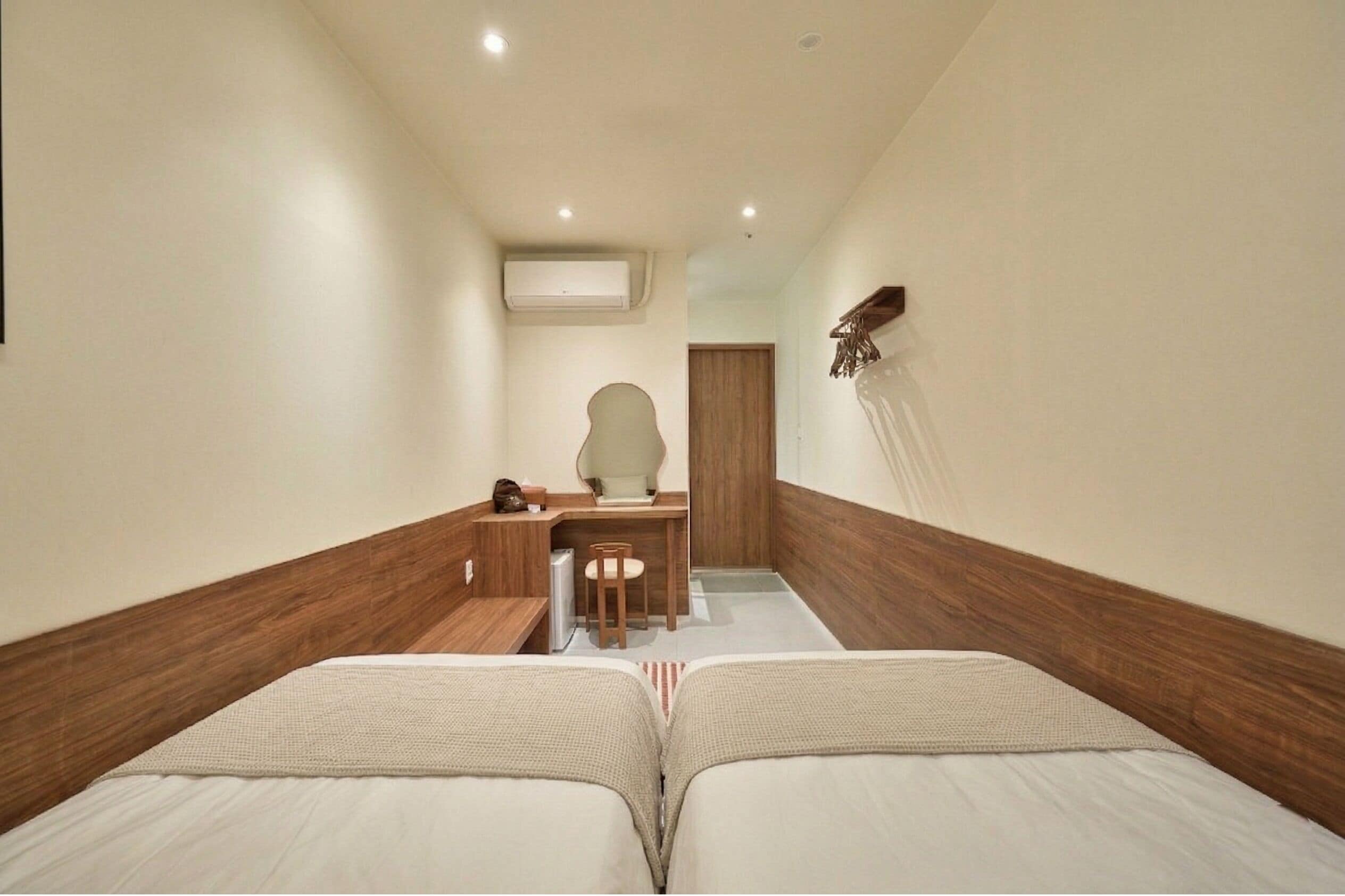 Habitación de hotel con dos camas, un escritorio, una silla, una mesita y un estante en la pared.