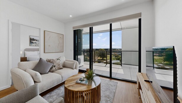A modern living room with a sofa, coffee table, and large windows offering a view of the outdoors. - Brand New 2 Bed Apartment with City Views (Cannington)