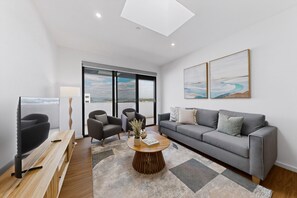Un salon moderne avec un canapé gris, deux fauteuils, une table basse et un téléviseur.