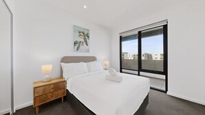 Habitació d'hotel moderna amb un llit gran, una taula de nit amb una làmpada, un quadre a la paret i una finestra gran amb vista a la ciutat.