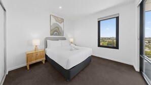 Ein modernes Hotelzimmer mit einem großen Bett, einem Nachttisch, einem Wandbild und einem Fenster mit Blick auf die Stadt.