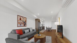 Ein modernes Wohnzimmer mit grauem Sofa, einem Holztisch und einem Essbereich mit Tisch und Stühlen.