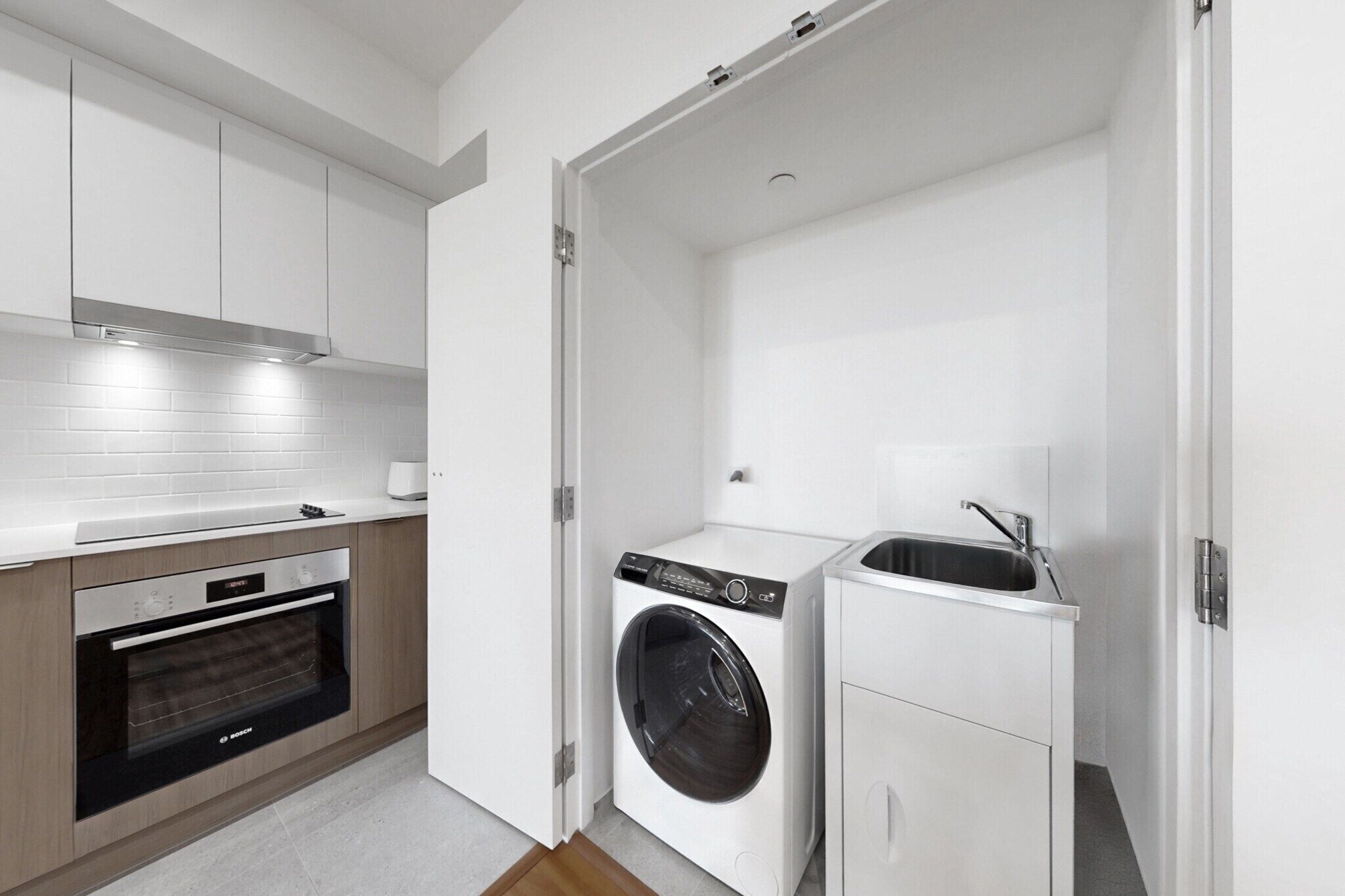 Une cuisine compacte équipée d’un four encastré, d’un lave-linge et d’un évier.