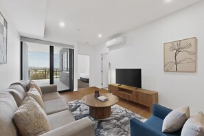A modern living room with a sofa, coffee table, TV, and artwork. - Bright Newly 2 Bed Apartment with Balcony Views (Cannington)