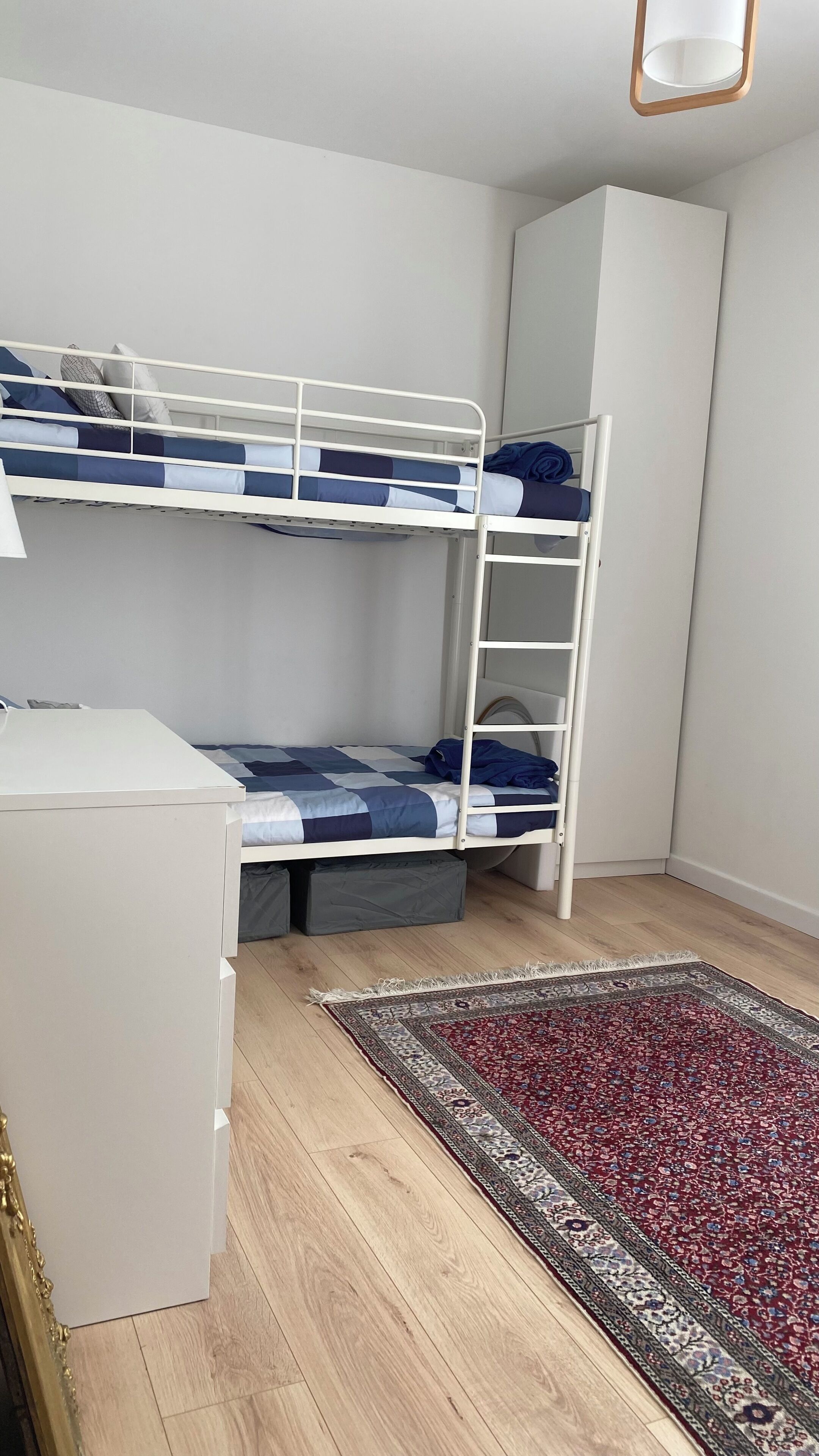 Una cama litera con estructura blanca, un escritorio pequeño blanco y una alfombra estampada sobre un suelo de madera.