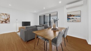 A modern living room with a wooden dining table, grey sofa, and a flat-screen TV.