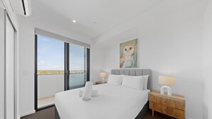 A modern hotel room with a large bed, a nightstand, a painting of an owl, and a view through the glass door.