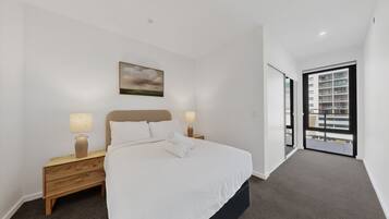 A bedroom with a bed, nightstands, a painting, and a view through a door.