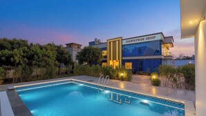 A swimming pool with a clear blue water, surrounded by a landscaped garden and a building labeled 'COUNTRYWIDE GROUP'. - Countrywide Corbett (Ramnagar)