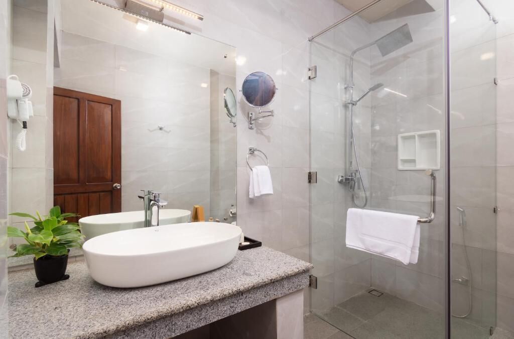 A modern bathroom with a freestanding sink, a glass shower enclosure, a wooden door, and a potted plant.