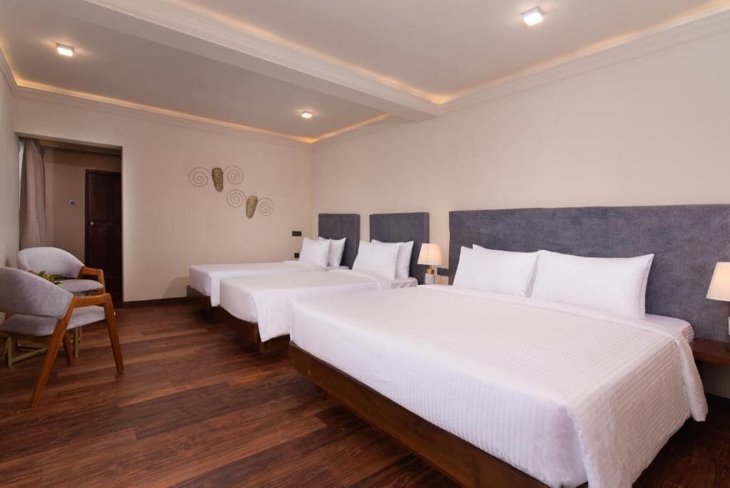 Une chambre d’hôtel avec trois lits, un plancher en bois, une chaise et une porte.