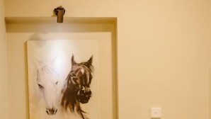 A room with a grey armchair, a round ottoman, and a wall-mounted painting of a horse. - Luxor Kirindi Ella Resort & Spa (Bandarawela)