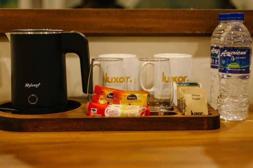 A tray with a black coffee maker, white mugs with 'luxar' branding, coffee packets, a sugar packet, and a water bottle.