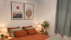 A neatly arranged bedroom with a bed, bedside tables, a hanging light fixture, and wall art.