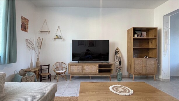A living room with a television, wicker furniture, a wooden cabinet, and a decorative surfboard.