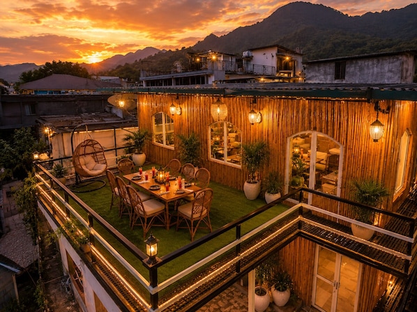A rooftop terrace with a dining area, potted plants, and a view of the sunset.