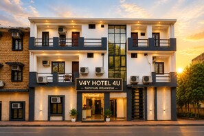 A modern hotel with a sign reading 'V4Y HOTEL 4U TAPOVAN RISHIKESH.' It features a two-story structure with balconies, large windows, and air conditioning units. - V4Y Hotel 4U Tapovan Rishikesh (Rishikesh)