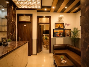 A hotel lobby with a reception desk, a sofa, a coffee table, a wall-mounted fan, and artwork.