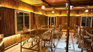 A dining area with a long table and wicker chairs, wooden walls, and warm lighting. - V4Y Hotel 4U Tapovan Rishikesh (Rishikesh)