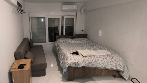 Ein Schlafzimmer mit einem Bett, einem Sofa, einem kleinen Tisch mit Telefon und Kiste sowie einem Fenster mit Jalousien.