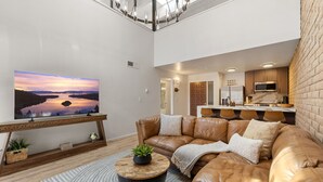Een moderne woonkamer met een leren bank, een flatscreen televisie en een keuken in de achtergrond.