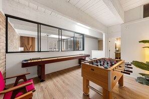 A room with a foosball table, a pool table, and a large window.