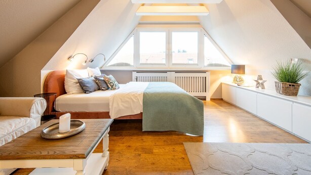 A cozy attic bedroom with a bed, bedside table, lamp, and a view through a window. - Princessa Coast - Holiday home "Princessa Coast" (Sylt)