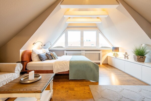 A cozy attic bedroom with a bed, bedside table, lamp, and a view through a window. - Princessa Coast - Holiday home "Princessa Coast" (Sylt)