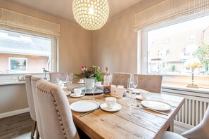 A dining table set for four with a bottle of liquor, glasses, and a vase of flowers. - Princessa Coast - Holiday home "Princessa Coast" (Sylt)