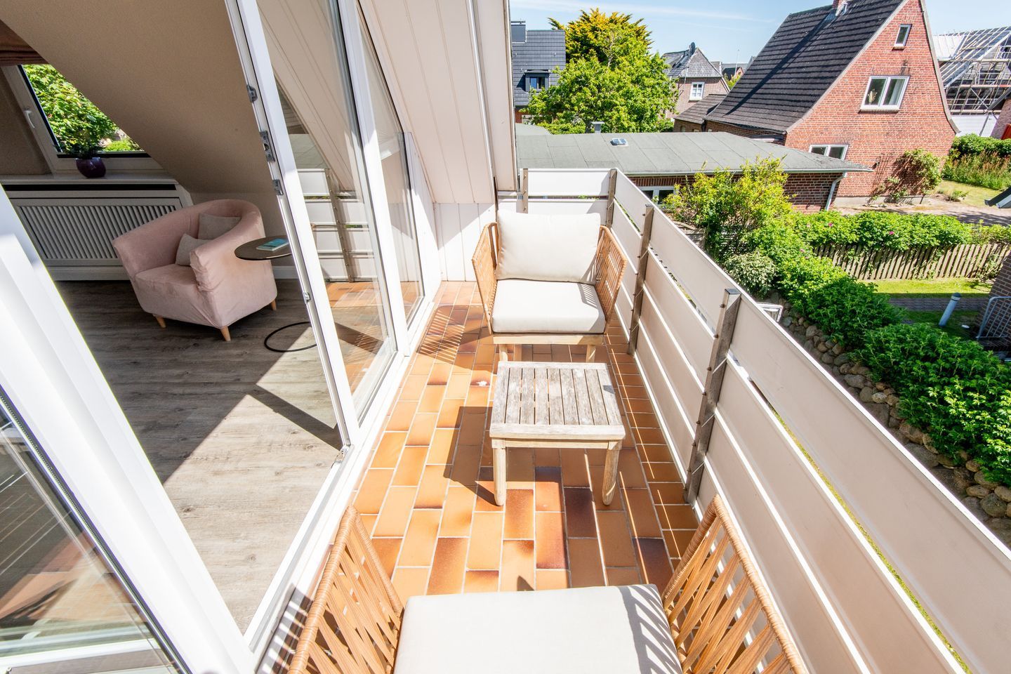 A balcony with a cushioned chair, a small table, and a view of the neighborhood.