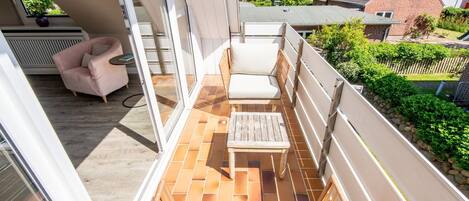 A balcony with a cushioned chair, a small table, and a view of the neighborhood.