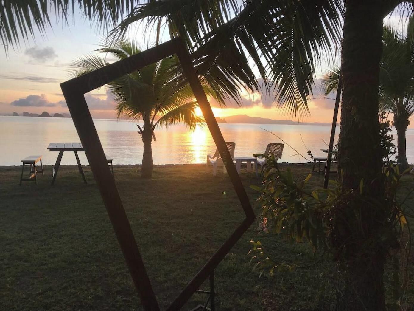 A beach scene with a sunset, palm trees, and outdoor furniture.