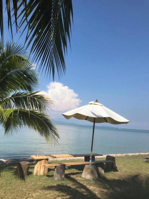 A beach scene with a wooden bench, a white umbrella, and a palm tree. - Koh Yao Yai Sea Breeze House (Ko Yao)