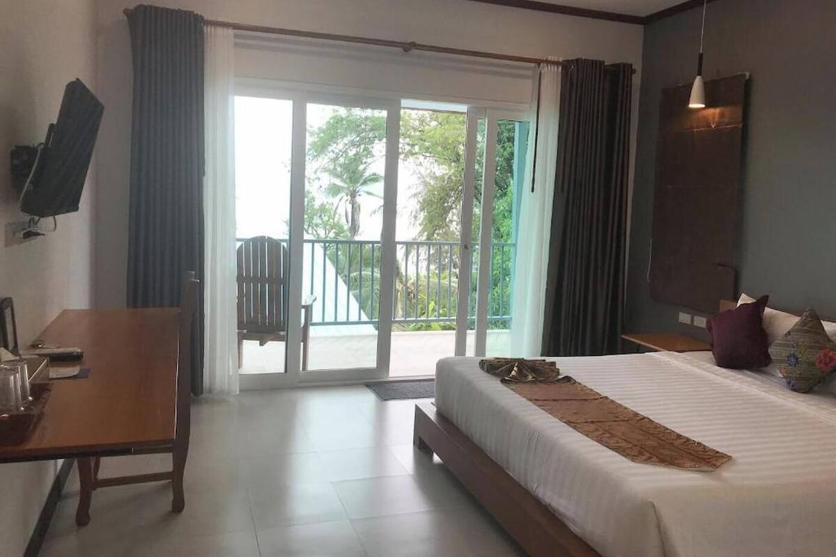 Une chambre d’hôtel équipée d’un lit, d’un bureau, d’une chaise, d’une télévision et d’un balcon donnant sur un espace verdoyant.