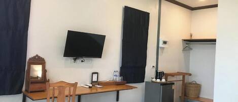 Une pièce de taille modeste, équipée d’un bureau, d’une chaise, d’une télévision et d’un petit réfrigérateur.